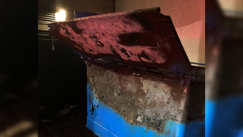 A blue dumpster is seen scorched by a fire, which has already been extinguished.