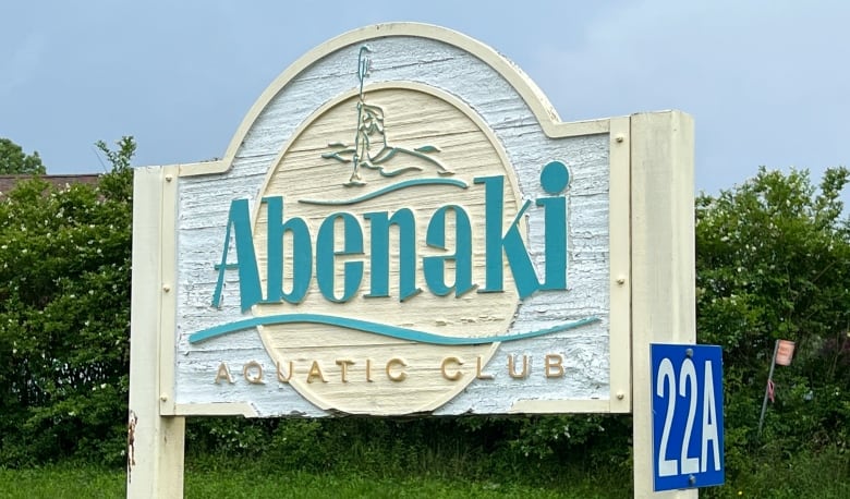 A large wooden beige, turquoise and gold sign reads 'Abenaki Aquatic Club.'