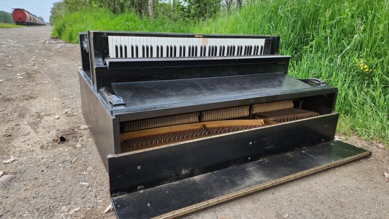 A damaged piano lies on the side of a dirt road.