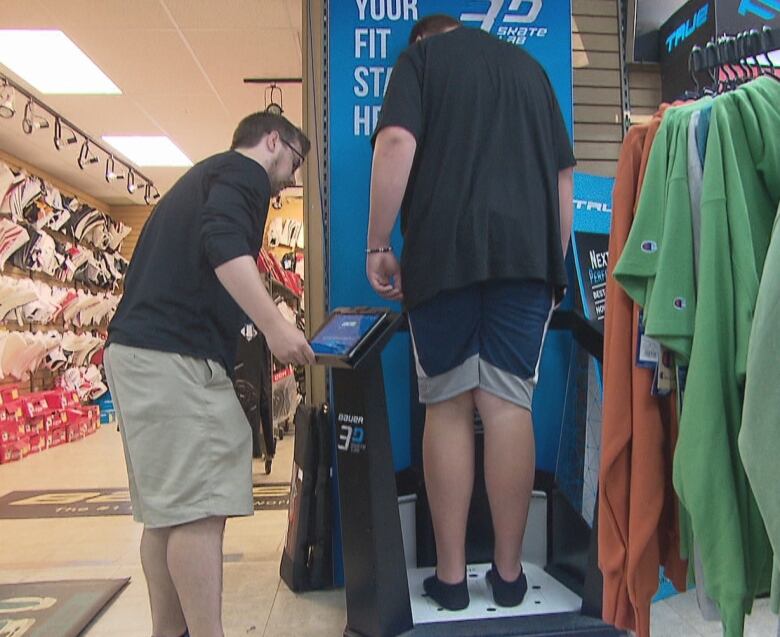 A man standing at a tablet attached to a machine and a tall boy standing on the base of the machine. 