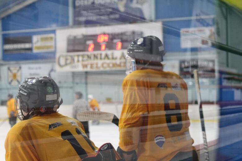 Two hockey players on the bench watch their teammates play.