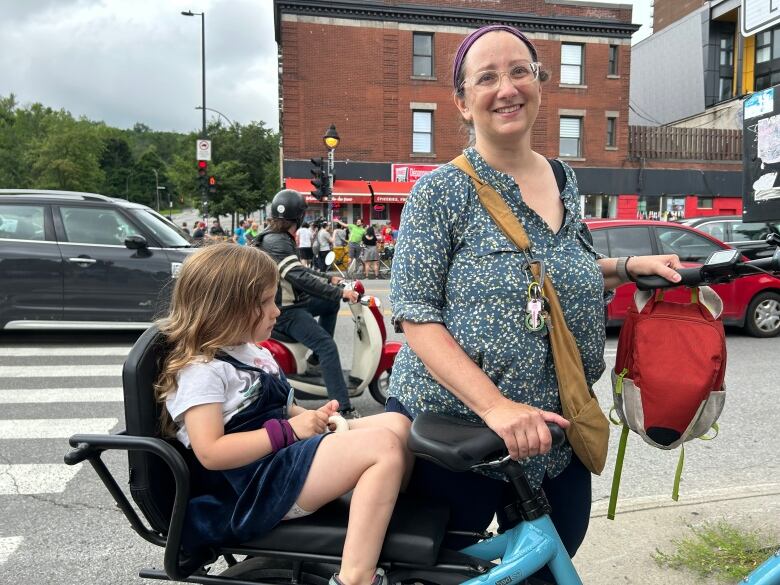 Picture of a woman participating in the human bike lane formed in Montreal's Parc Avenue. The woman stands behind her bike, her child is sitting on a toddler-seat at the back of the bike.