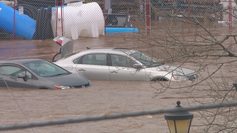 Two cars are submerged in water in a parking lot during a flood. One of them has an open trunk.