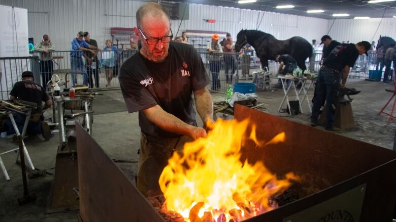 A blacksmith puts a horsehoe in a firery forge.