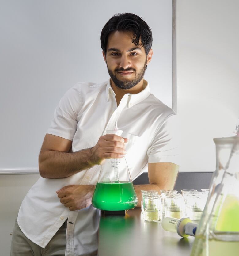 Ren Shahmohamadloo is an ecotoxicologist and postdoctoral scientist shown holding holding a flask of cyanobacteria.