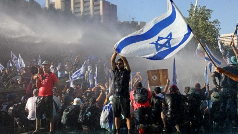 Protesters carry flags while water cannons are used nearby.