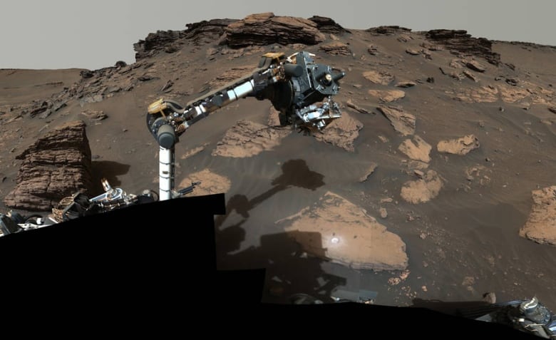 An arm on the Mars rover picks up a rock.