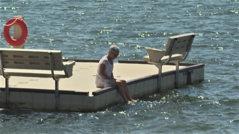 A woman sitting on the edge of the floating dock in Victoria Park.