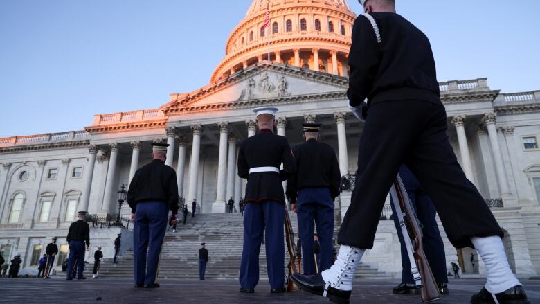 A reddish dawn rises over the U.S. Capitol, with several members of a military honour guard in the foreground