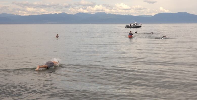 A man is seen diving into the ocean. In the distance is a boat and a kayak and another man swimming. 