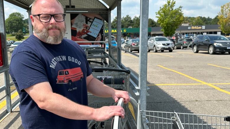 Mark Barrey in a parking lot with his hands on a shopping cart. 