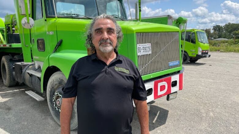 A middle-aged man with a beard standing in front of a green truck.