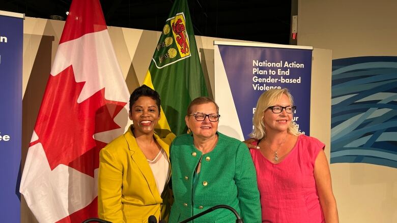 Three women stand in front of flags of Canada and Saskatchewan.