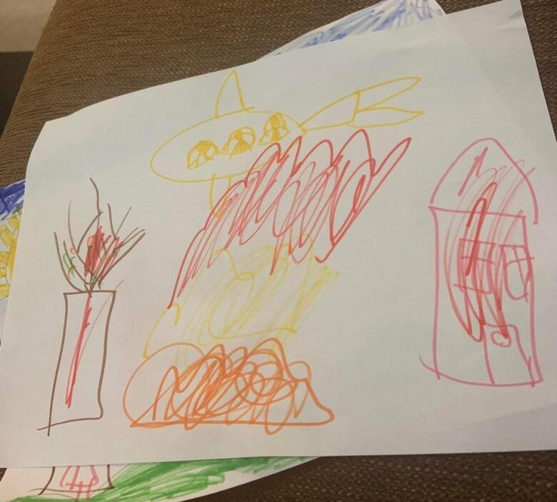 A children's drawing shows houses and buildings engulfed in flames as a helicopter hovers overheard. It's drawn on white paper in orange, red and yellow crayon.