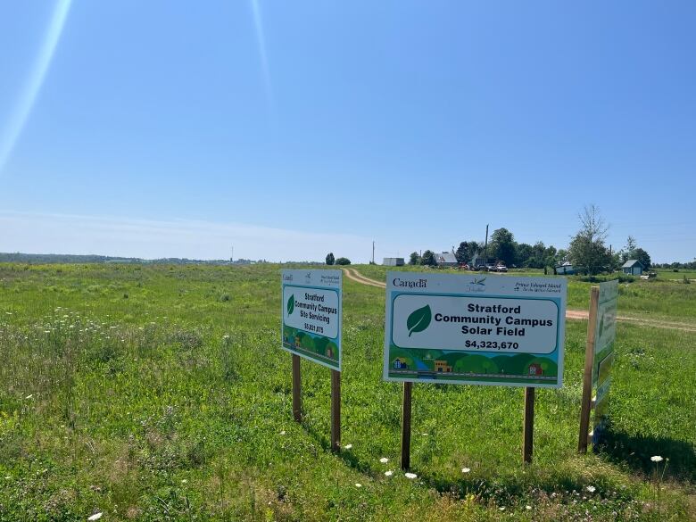 Three government signs sit in a large field of green grass.