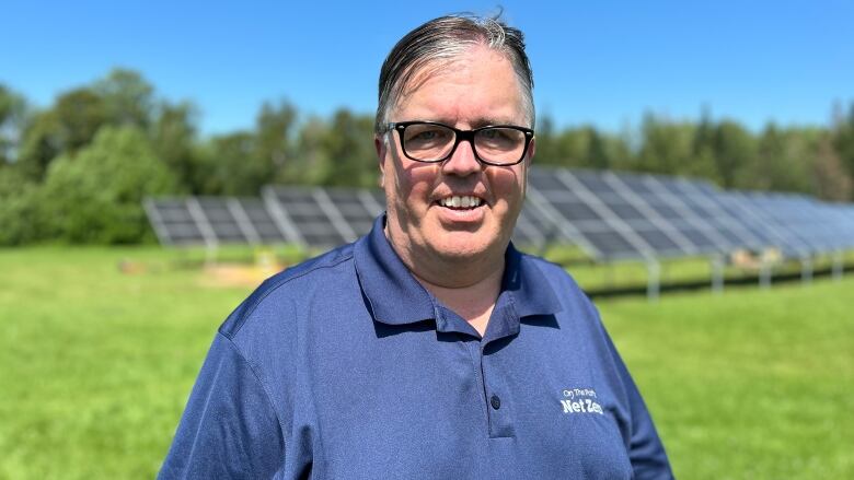 Steven Myers outside in summer in front of a field of solar panels.