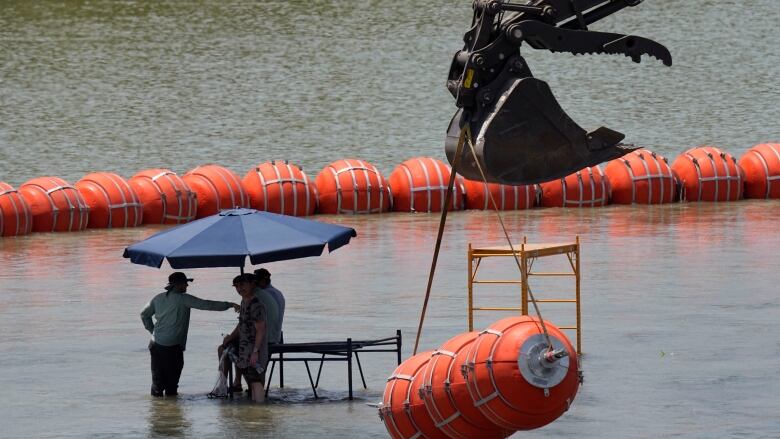 A large section of orange barrier is shown dangling in the air in the bucket of a crane.