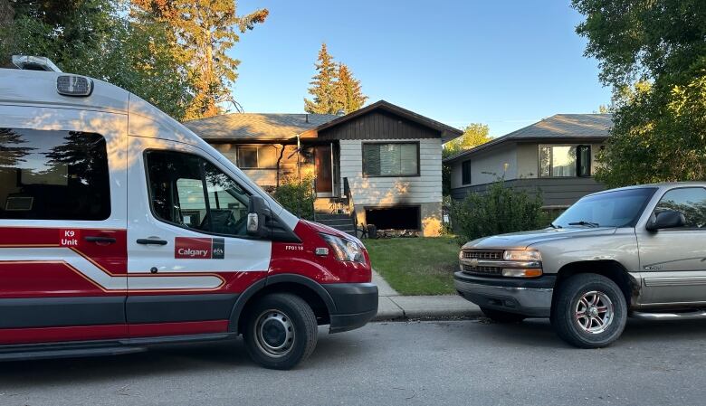 A fire department van sits parked outside the front of a house that has smoke and fire damage. 