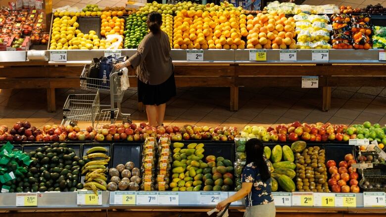 Two people by shopping carts in the fruit and vegetable section of a grocery store.