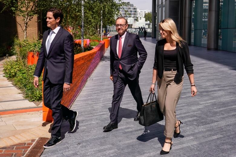 Two men and a woman dressed in businesswear walk outside on a sunny day.