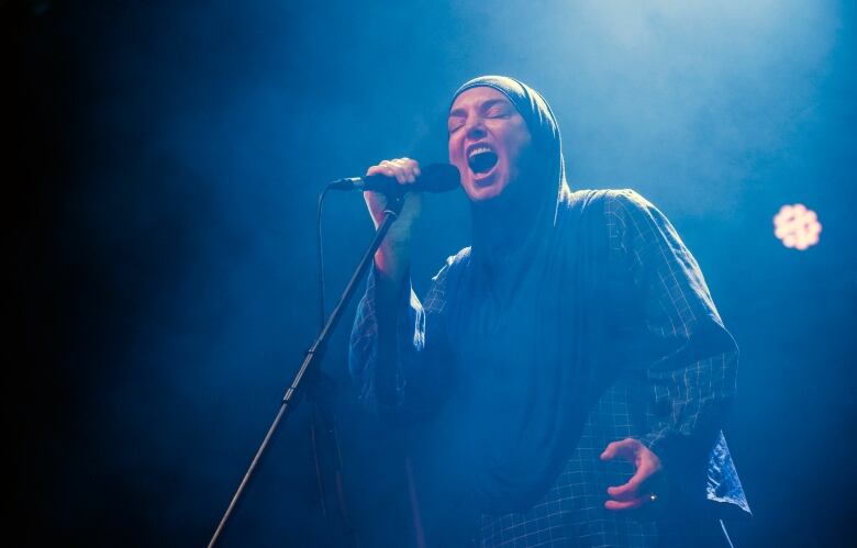 A singer in headscarf sings in front of a mic on stage.