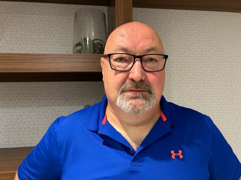 A man wearing a blue polo and glasses stares at the camera. 