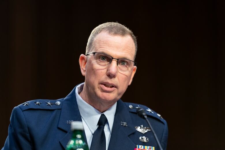 Man in blue military uniform with lots of medals, in front of dark background