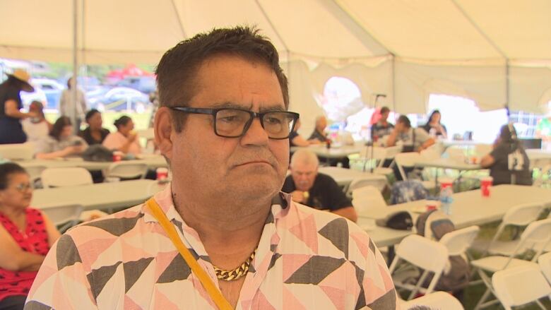 A man stands under a large white tent. People sit at tables behind him.