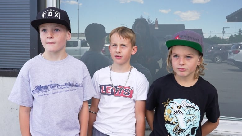 Three kids, aged seven to 10, in baseball caps and T-shirts, talk to someone off-camera.