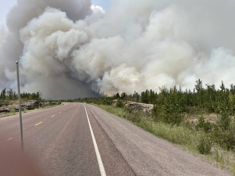 Wildfire smoke billows over a rural highway.