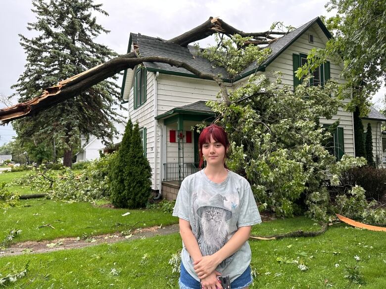 A girl with red hair stands in front of a house with a tree on it. 