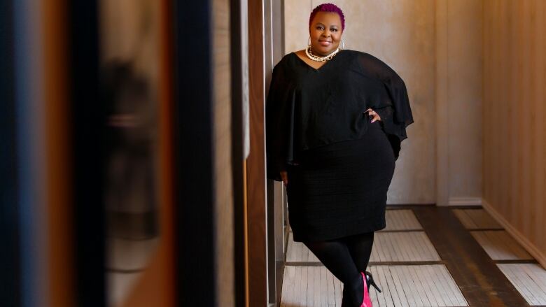 A woman stands in a court hallway wearing high heels with her arm on her waist. 