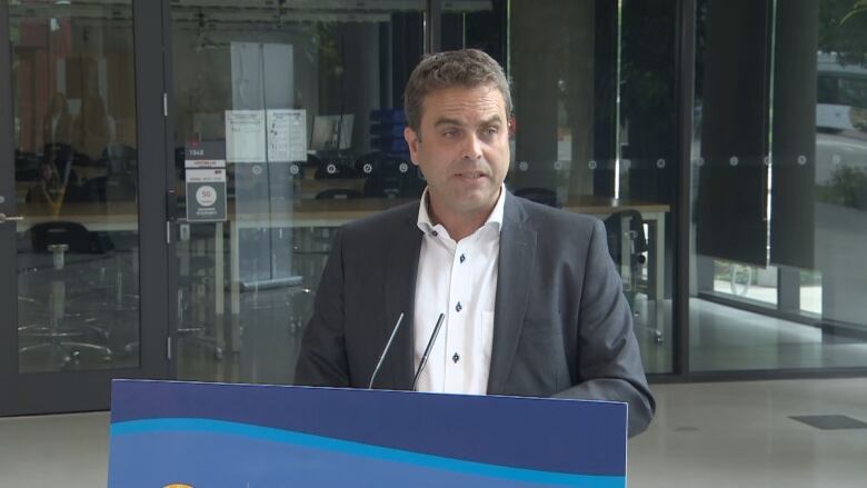 A man dressed in formals stands behind a podium giving a speech