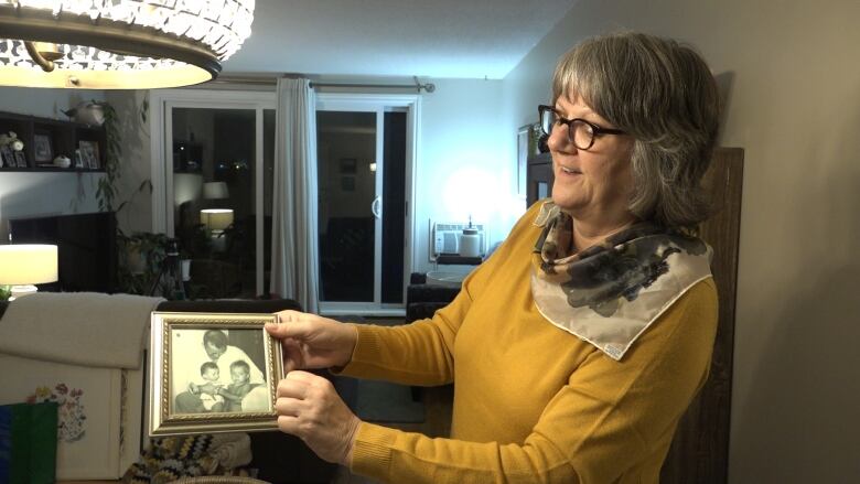 A woman in a yellow top looks at an old black and white photo of a man with two children.