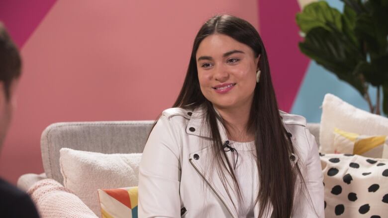 Actor, writer and director Devery Jacobs is seated on the couch on the set of Here & Queer.