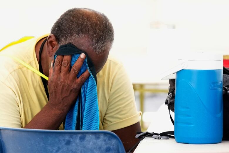 A man coping with heat wipes his face with a towel.