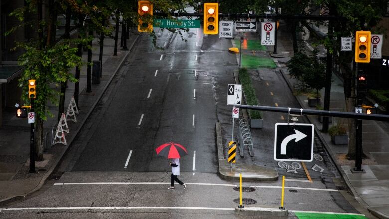 Person hidden by red umbrella walking at an intersection in downtown Vancouver.