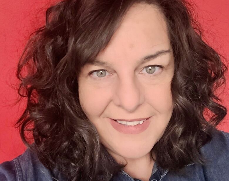 A woman in a denim shirt smiles for a portrait.