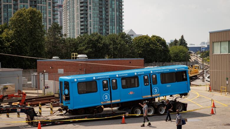 A blue rail car sits on top of a trailer bed inside a transit yard.