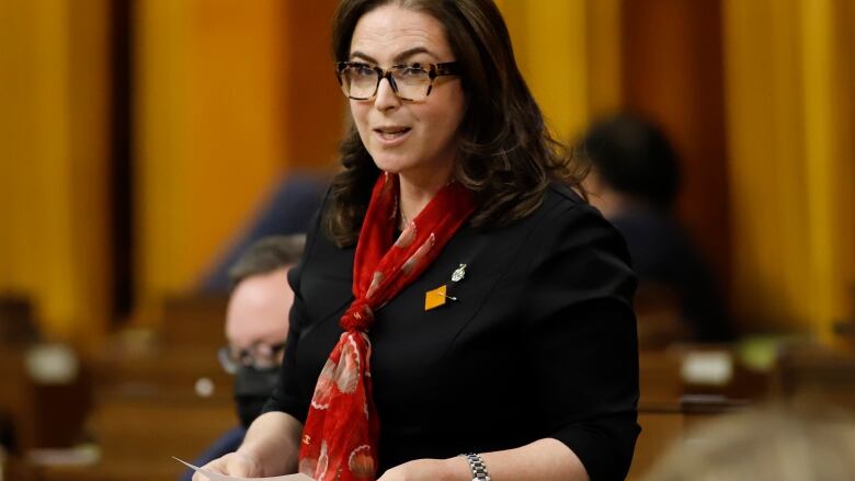 A woman wearing glasses stands in the House of Commons.