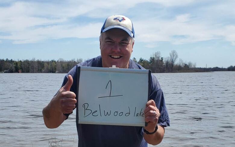 David stands in front of a lake holding a white board that reads 