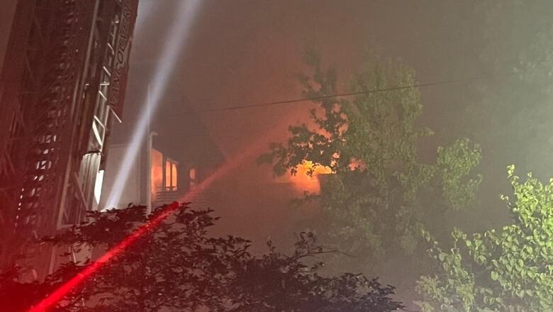 Glowing, orange flames are seen inside an apartment building burning at night. The dark sky is filled with gray smoke.