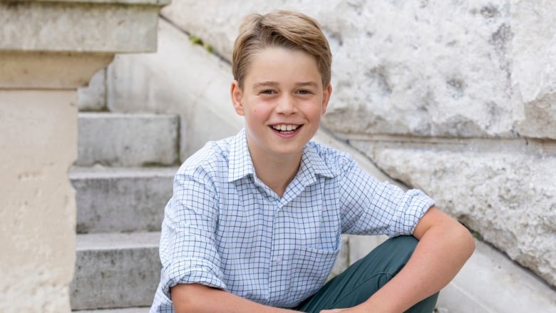 A young person smiles while sitting on steps beside a stone wall.