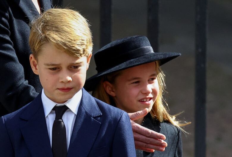 Two children walk in front of a fence.