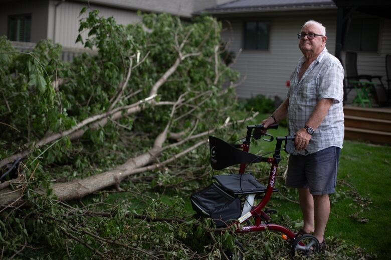 A man with a walker stands next to a downed tree