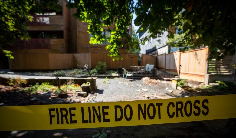 Yellow caution tape reads: Fire Line Do Not Cross. Behind it is debris scattered around an open space leading to an apartment building.