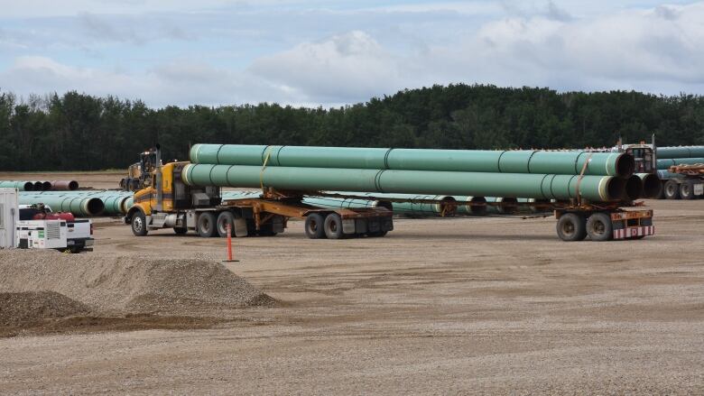  A heavy truck carrying long green pipe sits on a brown gravel surface.