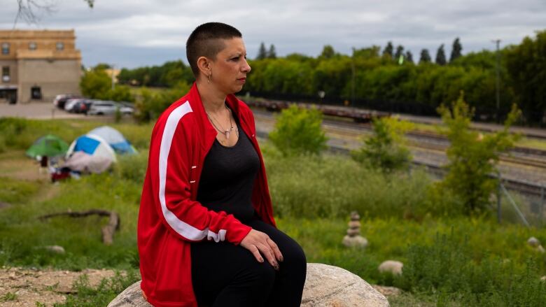 A woman sits on a rock looking at train tracks.