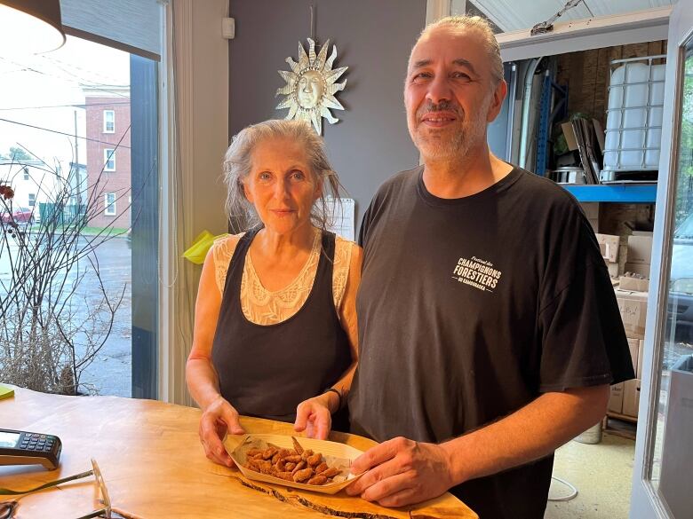 A couple stands behind a counter holding a plate of mushrooms. 