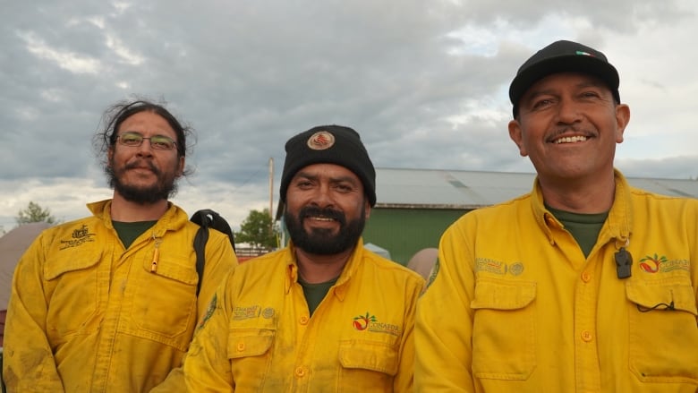 Three men stand shoulder to shoulder in yellow firefighting gear